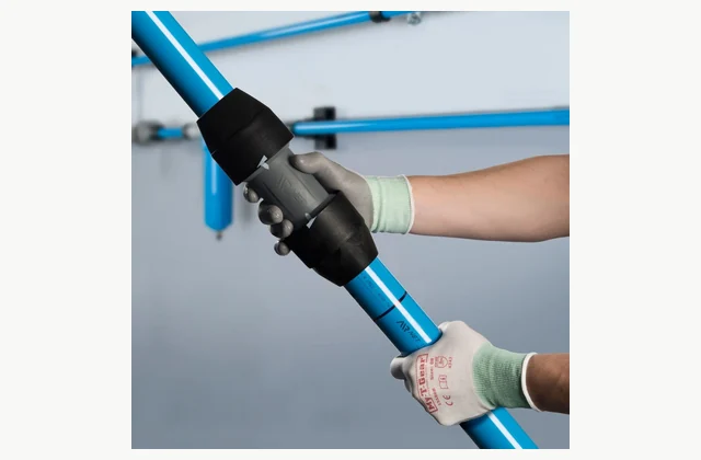 Real AIRnet aluminium compressed air pipes and mechanical coupling being assembled in front of an installed blue piping network